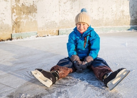 Symbolbild Eislaufen am Arlberg: kleiner Junge mit Schlittschuhen sitzt auf der Eislaufbahn in Zürs