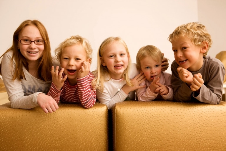 Symbolbild für Familien Hotel Kinderbetreuung: fünf lachende Kinder im Alter von 1 bis 12 Jahren knien auf einem Sofa im Österreichischen Oberlech am Arlberg