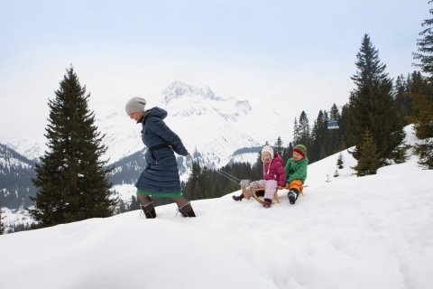 Rodeln in Österreich Symbolbild Rodeln in Österreich: eine Familie im Winterurlaub beim Rodeln in Österreich
