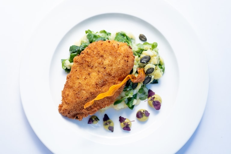 Zitronen-Backhendl auf Erdäpfel-Vogerl-Salat an Kürbiskernmayonaise und Kürbiskernöl auf weißem Teller