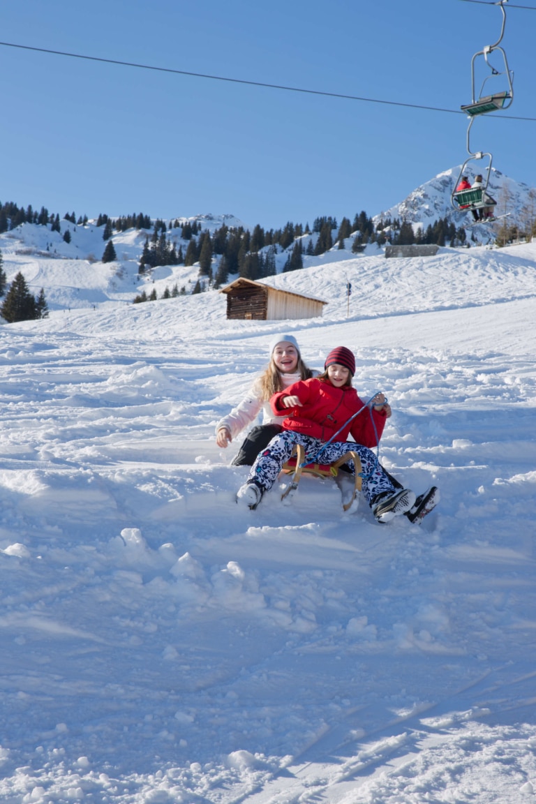 Zwei Mädchen fahren mit dem Schlitten im tiefen Schnee von Oberlech