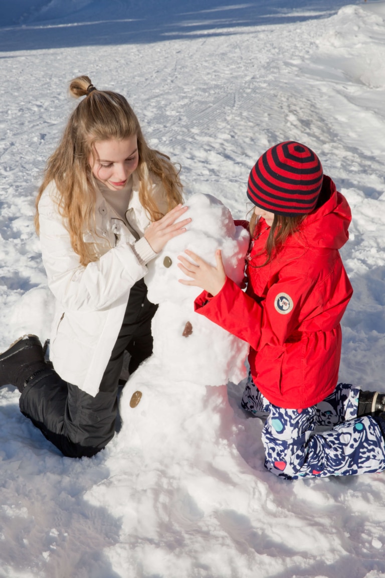 Zwei Mädchen knien im Schnee und bauen einen Schneemann