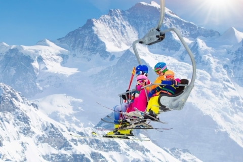 familie-im-sessellift_adobestock Familie sitzt im Sessellift, im Hintergrund ein verschneiter Gipfel