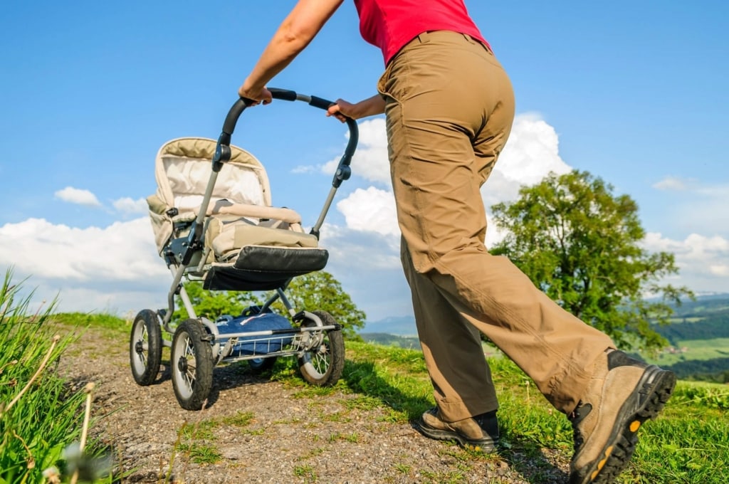 Wandern mit Kinderwagen: Mann im Wandergewand schiebt einen Kinderwagen über einen steinigen Wanderweg