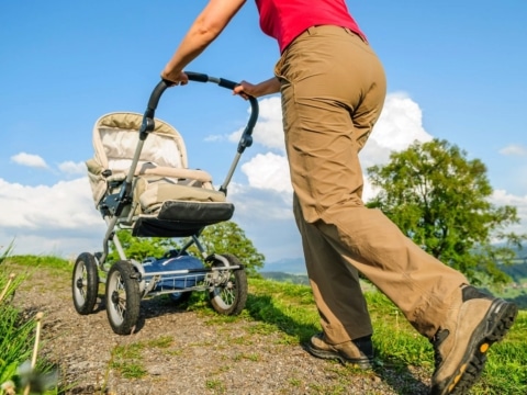 Wandern mit Kinderwagen: Mann im Wandergewand schiebt einen Kinderwagen über einen steinigen Wanderweg