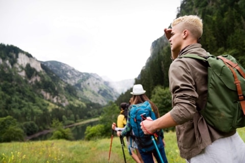 Aktivitäten_Sommer_Wandern_Teenager_Mann_Gruppe_Rucksack Familie mit Teenagern beim Wandern; sie gehen in einer Schlange, der letzte in der Reihe ist ein Jugendlicher mit blonden Haaren, der in die Ferne blickt