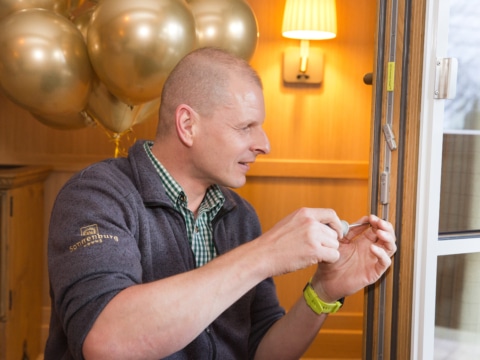 Sonnenburg_Familie_Mitarbeiter_Haustechnik_Tür_einstellen_Zimmer_2022_Ballons (1) Ein Handwerker bei der Wartung einer Fensterverriegelung in einem Hotelzimmer