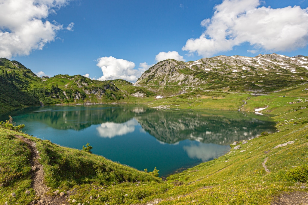 Symbolbild für Sommerurlaub in den Bergen: Formarinsee in Österreich umgeben von Wanderwegen und grünen Bergwiesen