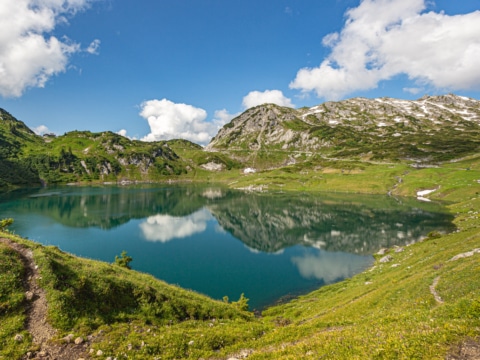 Symbolbild für Sommerurlaub in den Bergen: Formarinsee in Österreich umgeben von Wanderwegen und grünen Bergwiesen