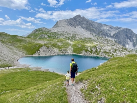 Sommerurlaub mit Kindern in den Bergen: Vater wandert mit Kind am Butzensee nahe Lech am Arlberg