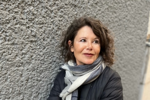 GabrieleKögl Frau mit Locken und Schal, die vor einer strukturierten Wand steht