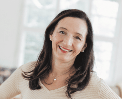 Petra Pellini (c) Nina Bröll_quer Eine freundliche Frau in einem hellen Raum mit natürlichem Licht lächelt herzlich in die Kamera.