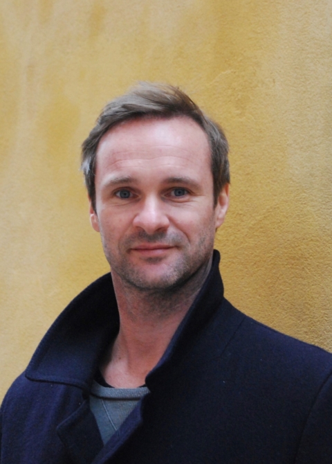 ClemensBerger Ein professioneller Mann in eleganter Oberbekleidung, steht vor einer gelben Wand, symbolisiert die Aufgeschlossenheit und Gastfreundschaft in der Tourismus- und Gastronomiebranche.