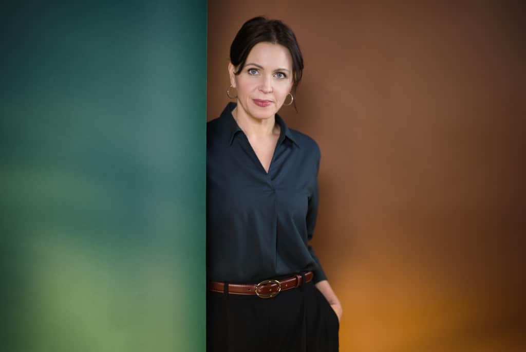 Jarka Kubsova, Deutsche Schriftstellerin Stehende Frau angelehnt an einer grünen Wand mit braunem Hintergrund.
