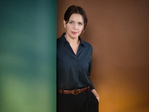 Jarka Kubsova, Deutsche Schriftstellerin Stehende Frau angelehnt an einer grünen Wand mit braunem Hintergrund.
